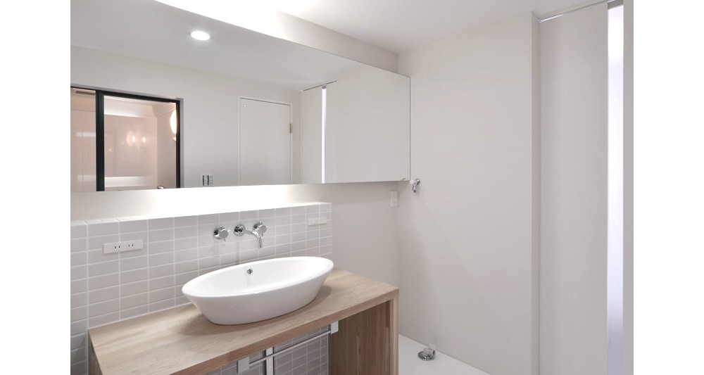 壁一面のミラーが広がりをもたらす落ち着いたトーンの洗面台