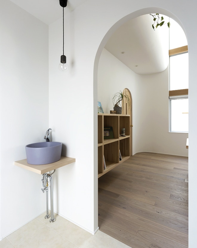 アーチ壁とくすみカラーの洗面ボウルがやわらかな印象をもたらす空間